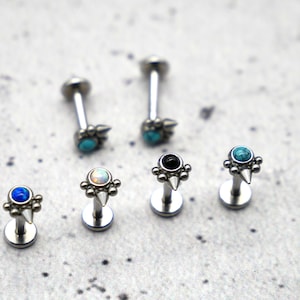 May include: Six silver body jewellery pieces with different coloured gemstones. The jewellery features a small spike and a cluster of small beads around the gemstone.