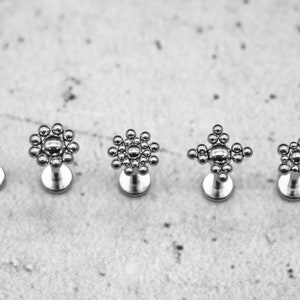 Könnte beinhalten: Fünf silberne Körperschmuckstücke mit verschiedenen kreisförmigen und sternförmigen Designs. Der Schmuck besteht aus kleinen, runden Perlen.