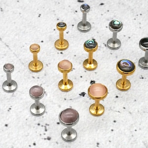 May include: Assortment of 14 gauge body jewelry with different colored gemstone tops. The jewelry is made of surgical steel and gold. The gemstones are pink, black, and iridescent.