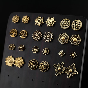 Op de afbeelding: Een display met 18 gouden oorbellen met verschillende geometrische en bloemmotieven. De oorbellen zijn in rijen op een zwart oppervlak gerangschikt.