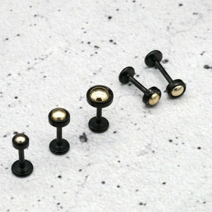 Könnte beinhalten: Fünf schwarze Barbell-Ohrringe mit goldenen Kugeln. Die Ohrringe sind nach Größe sortiert, von klein nach groß.