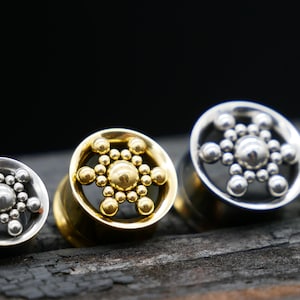 Puede incluir: Cinco expansores de oreja de diferentes tamaños con un diseño de copo de nieve dorado y plateado. Los expansores están hechos de metal y tienen un acabado brillante.