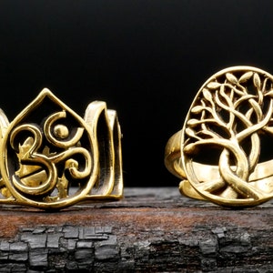 May include: Two gold-toned rings with intricate designs. One ring features the Om symbol within a lotus flower design. The other ring features a tree of life design.