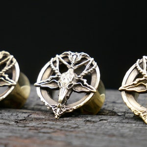 May include: Three brass ear gauges with a pentagram design featuring a goat's head in the center.