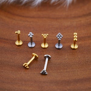 May include: A set of six silver and gold body jewelry pieces with different geometric designs. Each piece features a small bar with a decorative ball on each end.