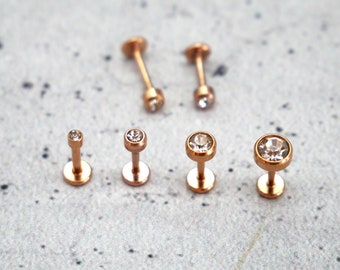 Può includere: Un set di sei gioielli per il corpo in oro rosa con accenti di cristallo trasparente. I gioielli sono disposti in fila su una superficie grigia.