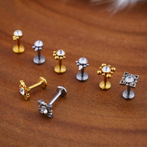 Peut inclure: Un ensemble de huit bijoux de corps argentés et dorés avec des accents de cristal transparent. Les bijoux présentent différents motifs, notamment une étoile, un carré et un cercle.