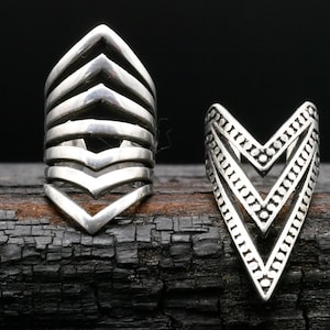 May include: Two silver geometric rings with a chevron design. The ring on the left has five layers of chevrons, while the ring on the right has two layers of chevrons with a dotted pattern.