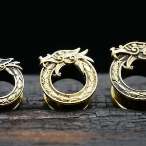 May include: Three gold-coloured dragon-shaped ear gauges of different sizes. The gauges are made of metal and have a detailed design.