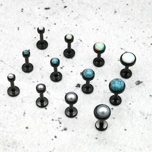 May include: A collection of 13 black surgical steel body jewelry pieces with various colored gem tops. The gems include turquoise, white, and iridescent.