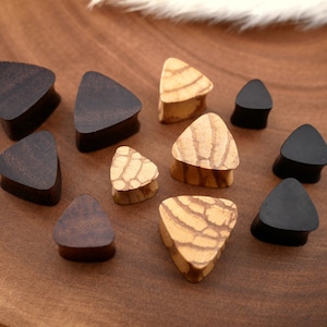 May include: A collection of triangular wooden ear gauges in various shades of brown and natural wood with a patterned design.