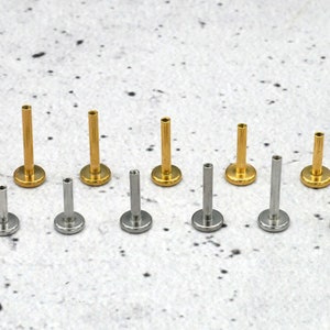 May include: A set of 10 gold and silver body jewellery pieces. The jewellery is in different sizes and is arranged in a row on a white surface.