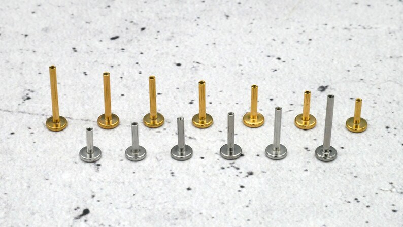 May include: A set of 10 gold and silver body jewellery pieces. The jewellery is in different sizes and is arranged in a row on a white surface.