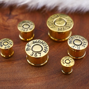 May include: Six gold-colored bullet-shaped earrings with the text "R.F. 357 MAGNUM" on each.