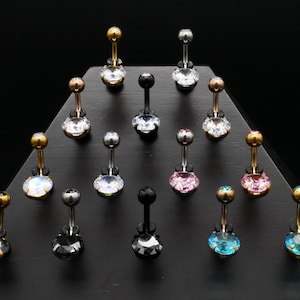 May include: A selection of belly button rings with various coloured gems, including clear, pink, blue, and black. The rings are displayed on a black stand.