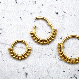 Könnte beinhalten: Drei goldfarbene Körperschmuckringe mit einem Perlenmuster. Die Ringe sind in verschiedenen Größen und auf einem weißen Hintergrund angeordnet.