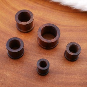 May include: Set of five wooden ear gauges in various sizes. The gauges are brown and have a smooth, polished finish.