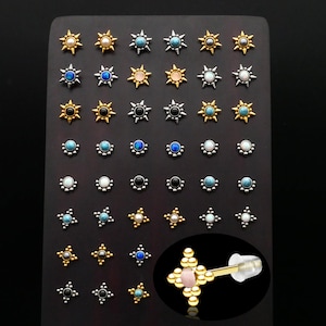 May include: A display of various gold, silver, and black star-shaped body jewelry with different colored gemstones. The jewelry is arranged on a black display board.