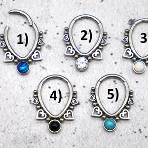 Puede incluir: Cinco anillos de septum de plata con un dise&ntilde;o de coraz&oacute;n y piedras preciosas de diferentes colores. Los anillos est&aacute;n numerados del 1 al 5.