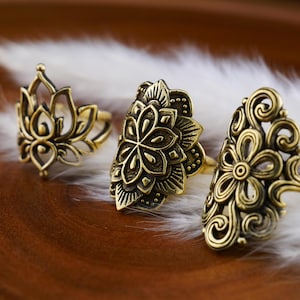 Könnte beinhalten: Drei goldfarbene Ringe mit filigranen Blumenmustern. Die Ringe sind aus Metall und haben einen Vintage-Look.