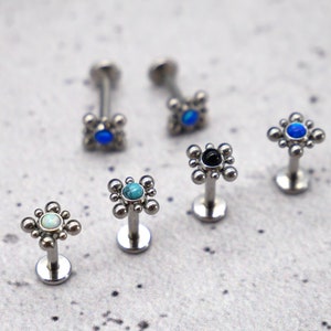 May include: Six silver body jewelry pieces with a square design and a single gemstone in the center. The gemstones are blue, turquoise, black, and white.