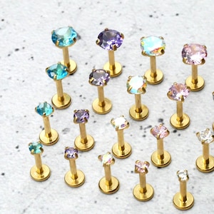 May include: A variety of gold-toned body jewelry with different colored gems. The gems are in shades of blue, purple, pink, and clear.
