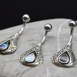 May include: Three silver belly button rings with ornate teardrop-shaped charms. Each charm features a different colored abalone shell inlay.