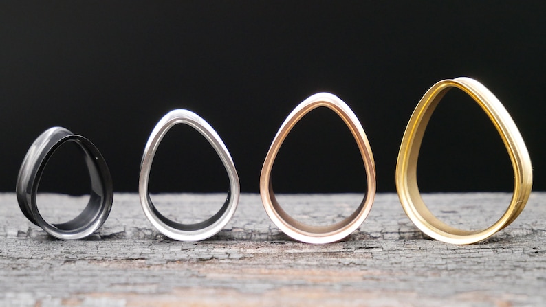 May include: Four different sized, oval-shaped, metal ear gauges. The gauges are black, silver, rose gold, and gold.