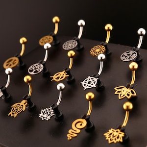 Könnte beinhalten: Eine Sammlung von Bauchnabelpiercings in Gold- und Silbertönen. Die gebogenen Stäbe haben dekorative Anhänger, darunter eine Schildkröte, eine Lotusblume und verschiedene geometrische Designs. Der Schmuck wird auf einer schwarzen Oberfläche präsentiert.