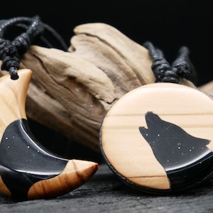 Könnte beinhalten: Zwei Holzketten mit schwarzen Harzeinlagen. Eine Kette hat die Form einer Mondsichel und die andere zeigt einen Wolf, der zum Mond heult.