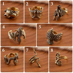 Pode incluir: Uma coleção de oito anéis de metal em tom dourado com vários designs de animais e criaturas, incluindo um lobo, morcego, polvo, dragão, águia e cobra, cada um com um estilo de banda aberta para ajuste regulável no dedo.