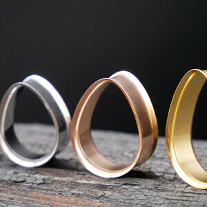 May include: Four teardrop-shaped ear gauges in different finishes: black, silver, rose gold, and gold.