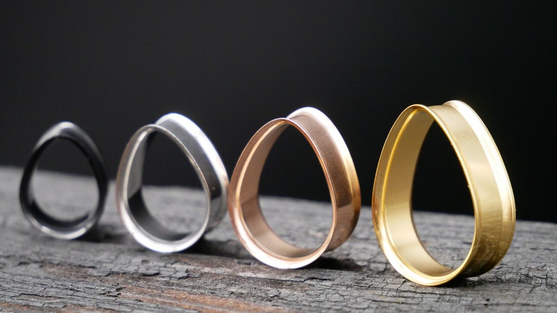 May include: Four teardrop-shaped ear gauges in different finishes: black, silver, rose gold, and gold.