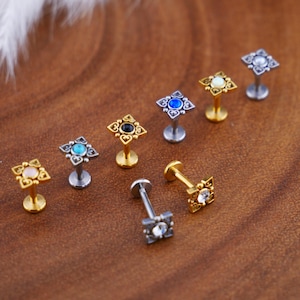 Può includere: Assortimento di 10 pezzi di gioielleria per il corpo in oro e argento con disegni decorativi e pietre preziose colorate. Ogni pezzo presenta una base quadrata con un design decorativo e una singola pietra preziosa al centro. Le pietre preziose sono blu, nere, bianche e turchesi.