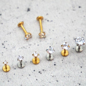 May include: A set of nine clear crystal stud earrings with gold and silver posts. The earrings are arranged in a row from smallest to largest.