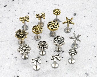 May include: Assortment of 15 silver and gold body jewelry pieces. The jewelry features a variety of designs including bows, flowers, stars, and geometric shapes. The jewelry is displayed on a white background.