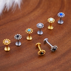 Peut inclure: Assortiment de huit bijoux de corps en or et en argent avec des dessus en forme de fleur présentant des pierres précieuses de différentes couleurs. Chaque pièce a un petit poteau pour le perçage.