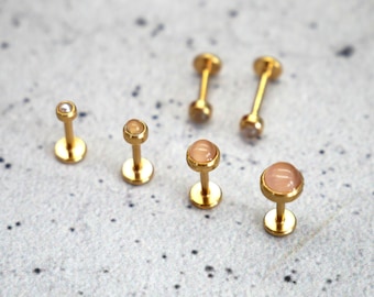 Puede incluir: Seis piezas de joyería corporal de oro con piedras de diferentes colores. Dos piezas tienen piedras transparentes, dos tienen piedras rosa claro y dos tienen una piedra rosa más oscura.