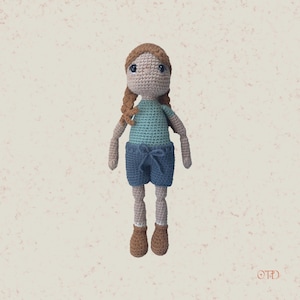 Op de afbeelding: Een gehaakte pop met bruin haar, blauwe ogen, een turquoise shirt, blauwe shorts en bruine schoenen.