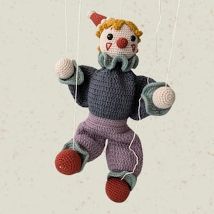 Peut inclure: Marionnette clown en crochet faite à la main. Le clown a un nez rouge, des chaussures rouges et un petit chapeau rouge et blanc. Le corps est bleu-gris, le pantalon lavande et les cheveux jaunes. Suspendu par des fils blancs.