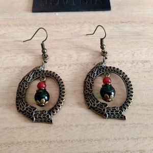 May include: A pair of bronze earrings with a green and red bead hanging from each. The earrings are in the shape of a circle with a detailed design.