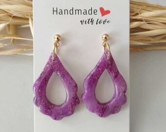 May include: A pair of handmade purple teardrop earrings with gold-colored accents. The earrings have a scalloped edge and a gold-colored stud. The card behind the earrings says "Handmade with love."