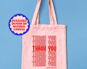 May include: A pink canvas tote bag with the words "THANK YOU" repeated in red. The phrase "HAVE A NICE DAY" is printed at the bottom. The bag is hanging against a blue background.