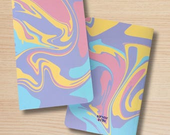 May include: Two notebooks with a colorful, swirled design in shades of pink, yellow, blue, and purple. The front notebook is labeled "FRONT" and the back notebook is labeled "BACK" with the brand name "barnesby & fox". The notebooks are on a light wood surface.