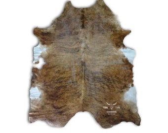 May include: Brown and white cowhide rug with a natural, rustic look. The rug has a unique pattern of brown and white patches. The rug is made of real cowhide and has a soft, luxurious feel.
