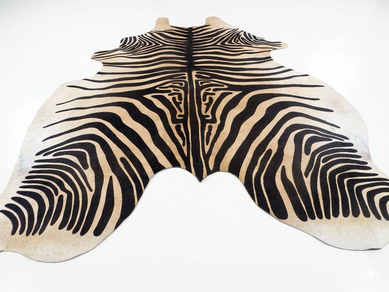 May include: A zebra-print rug with a beige background and bold black stripes. The rug has an irregular shape, mimicking the form of an animal hide. The design features a symmetrical pattern, creating a striking visual effect. This decorative rug is suitable for home decor.