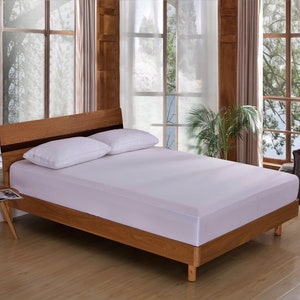 May include: A white mattress with a wooden bed frame. The bed is made with two white pillows and a white bedspread. The bed is in a room with large windows and wooden walls.