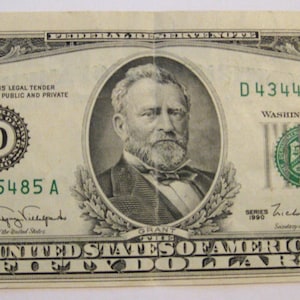May include: A fifty-dollar bill featuring a portrait of Ulysses S. Grant. The bill has green and black ink with the text "UNITED STATES OF AMERICA" and "FIFTY DOLLARS". The serial number is D43445485A.