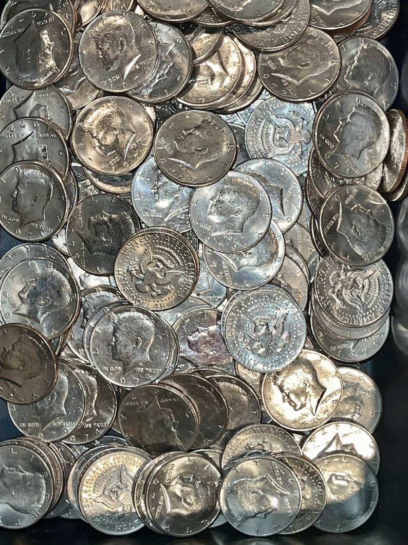 May include: A close-up shot of a pile of silver Kennedy half-dollar coins. The coins are scattered, showing the profile of John F. Kennedy and the words "IN GOD WE TRUST" and the year 1972 or 1971.