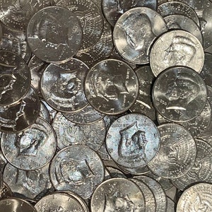 May include: A close-up shot of a pile of silver half-dollar coins. The coins feature the profile of a man on one side and an eagle on the other. The coins are scattered, with some partially visible.